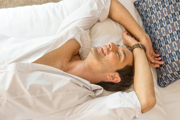 Красивый молодой человек улыбается и отдыхает на кровати отеля — стоковое фото