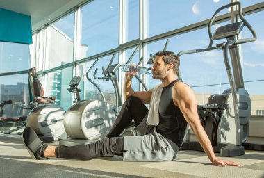 Yakışıklı zinde adam spor salonunda su içiyor.
