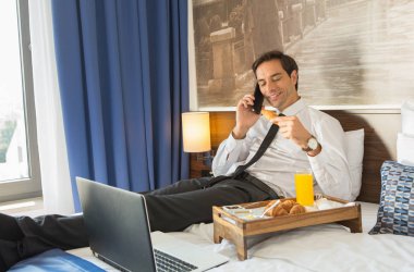 Takım elbiseli mutlu işadamı otel yatağı üzerinde çalışıyor.