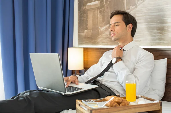 Vermoeide zakenman in pak werkend op het hotelbed op zijn comput — Stockfoto