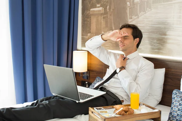 Müder Geschäftsmann im Anzug arbeitet am Hotelbett auf seinem Computer — Stockfoto