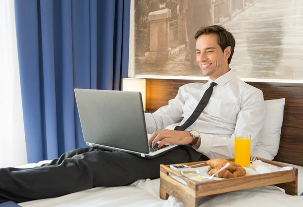 Glücklicher Geschäftsmann im Anzug, der am Hotelbett auf seinem Computer arbeitet — Stockfoto