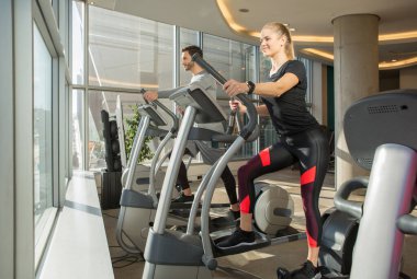 Modern spor salonunda kişisel fitness eğitmeniyle ekipmanlı kadın eğitimi.