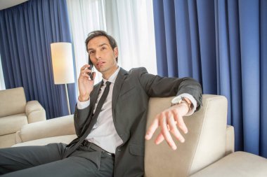 İşadamı otel odasında cep telefonuyla konuşuyor.
