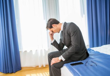 Hüsrana uğramış iş adamı otel yatağında oturmuş elini başının üstünde tutuyor.