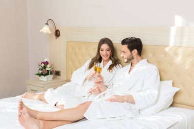 Bir otel odasında şarap içen bornozlu çekici genç bir çift.