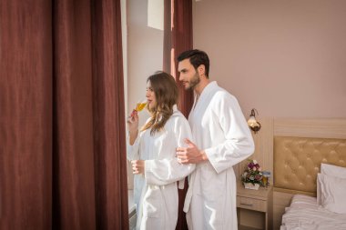 Otel odasında şarap içen bornozlu çekici genç bir çift.