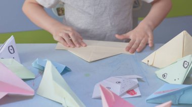 6 yaşındaki çocuk Covid-19 karantinası sırasında origami uçakları ve kurbağalar üretiyor. Kendini tecrit, online eğitim, evde eğitim. Çocuk evde, çocuk bahçesi kapalı, çocuk sanatı.