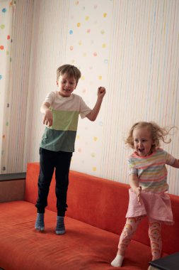 İki mutlu çocuk evde yastık savaşı yapıyor. Aile eğlencesi. Beyaz erkek ve kız kardeşler yatak odasında. Coronavirüs salgını sırasında karantina covid-19 ve kapalı okul.