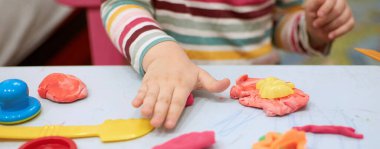 Child hands playing with colorful clay. Plasticine. play dough, social distance quarantine Covid-19, self-isolation, online education concept, homeschooling. Toddler girl at home, kindergarden closed. clipart