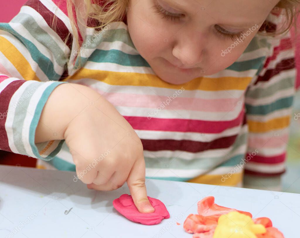 Child hands playing with colorful clay. Plasticine. play dough, social distance quarantine Covid-19, self-isolation, online education concept, homeschooling. Toddler girl at home, kindergarden closed.