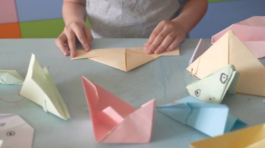 6 yaşındaki çocuk Covid-19 karantinası sırasında origami uçakları ve kurbağalar üretiyor. Kendini tecrit, online eğitim, evde eğitim. Çocuk evde, çocuk bahçesi kapalı, çocuk sanatı.