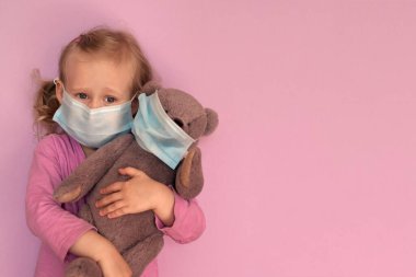 Yüz maskeli oyuncak ayılı kız. Beyaz çocuk Coronavirus Covid-19 salgını sırasında yüz maskesi takıyor. Evde kal, sosyal mesafeyi koru, kendini izole et. karantina sırasında.