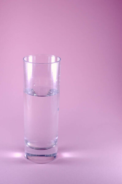 Glass of water isolated on pink coloured background with sprig first flower blossom. Sping minimal concept. Womens Day, Mothers Day, Valentine's Day, Easter, birthday. Nature background, isolated, flat lay, copy space.