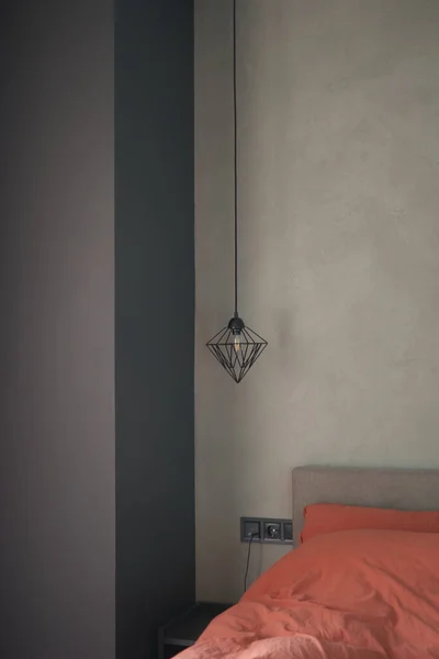 Decorative lamp hanging from the ceiling near the bed. Minimalist interior design. Stylish bedroom and livingroom. Grey stone wall in a designer minimalist room furniture.
