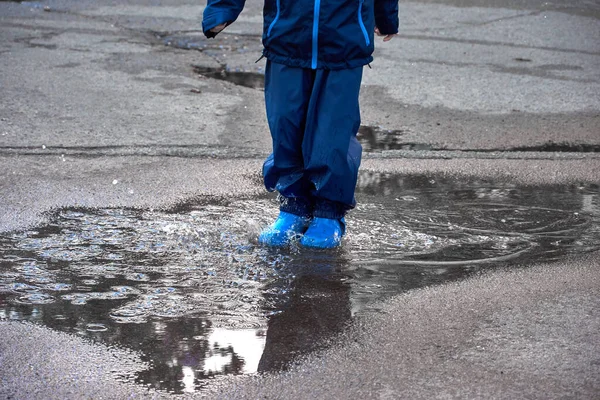 Feliz niño saltando en charco en abrigo impermeable. Un niño se divierte en el clima lluvioso con un impermeable brillante . — Foto de Stock