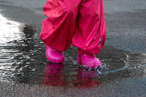 Feliz niño saltando en charco en abrigo impermeable. Una chica se divierte en el tiempo de lluvia en un impermeable brillante . — Foto de Stock