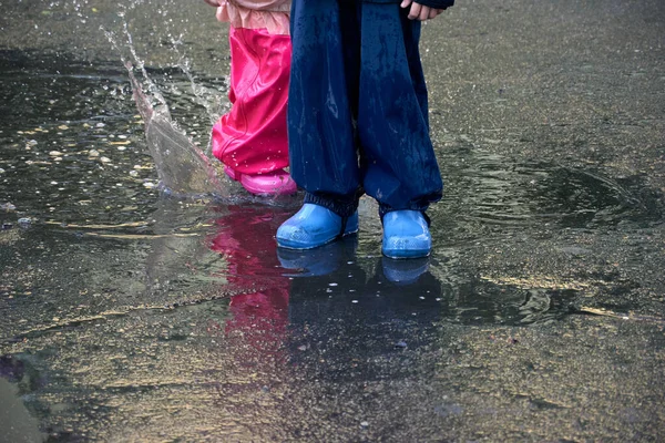 Happy children jumping in puddle in waterproof coat. Boy and girl have fun in the rain weather in a bright raincoat.