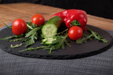   ,  ,  ,       .  . Taze vişneli domates, kırmızı biber, dilimlenmiş salatalık, siyah tabakta roka salatası. Taze sebze..