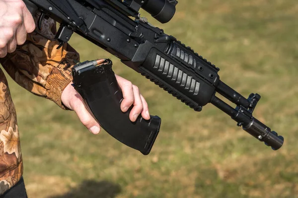 A man is holding a rifle magazine camouflage clothes