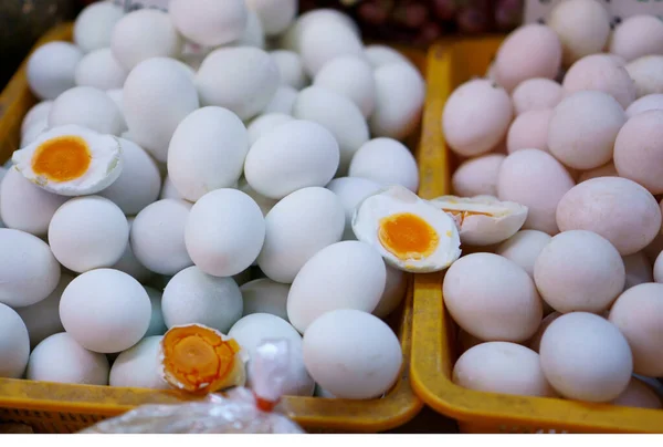 White round salted duck eggs in yellow plastic basket, half sliced eggs with yolk, albumen on top and fresh eggs on the right