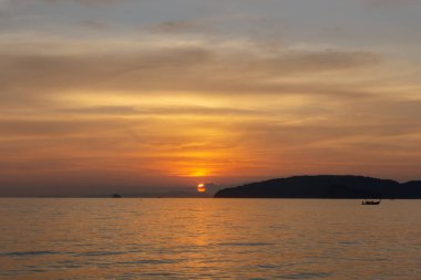 Akşamüstü bulutlu gökyüzünde parlayan turuncu ışığın güzel manzarası akşam vakti Tayland, Krabi 'de bir plajda deniz ve siyah dağ üzerindeki alacakaranlık sahnesine dönüşür.