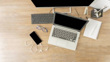 Siyah ekran dizüstü bilgisayar, klavye, cep telefonu, not defteri, ofisteki kalem kutusu gibi ahşap çalışma masasının üst görüntüsü