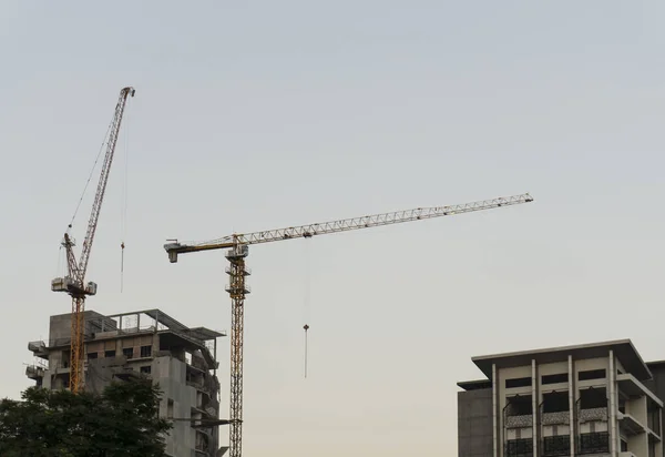 Two yellow steel tower crane standing beside the buildings that on construction, on cloudy sky background