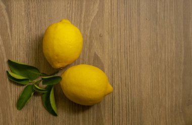 Üst görüntü, taze sarı olgun limon meyveleri ve kahverengi ahşap masada yeşil yaprak ve kopyalama alanı.