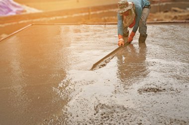Güneş ışığı altında yere beton yapıştıran bir işçi.