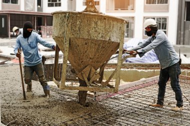 Erkek işçiler zemine beton döküyor.