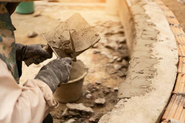 Tuğla duvara güneş ışığı altında sıva yapan bir işçi