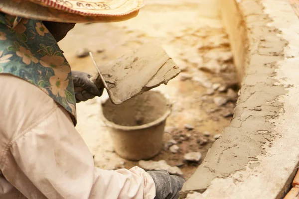 Tuğla duvara güneş ışığı altında sıva yapan bir inşaatçı.
