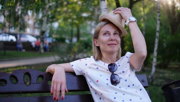 Junge erwachsene Frau sitzt mit Hut in der Hand auf der Parkbank. — Stockfoto
