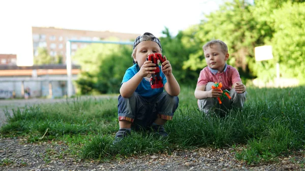 Zwei süße kleine Jungen mit Spielzeug sitzen im Gras auf dem Spielplatz — Stockfoto