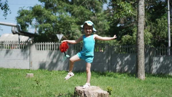 Una bambina sta su una gamba su un ceppo in un parco con una bambola in mano — Foto Stock