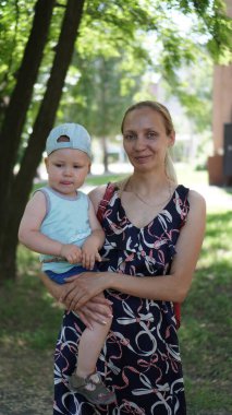 Mavi tişörtlü küçük çocuk ve parkta çimenlikte annesi.