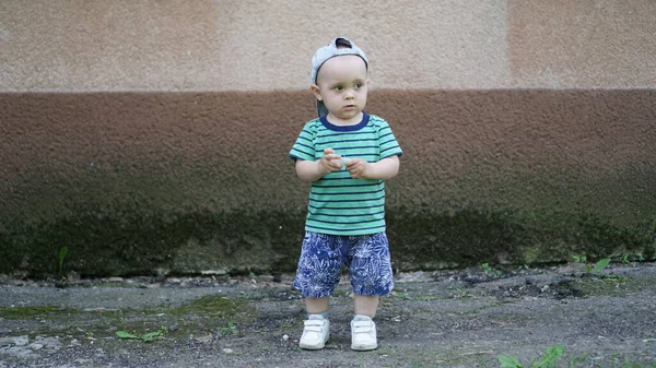 Petit garçon en T-shirt vert et chapeau seul près du mur plâtré — Photo