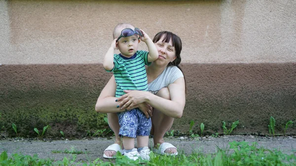 Engraçado bebê e sua mãe agachamento abraçando-o — Fotografia de Stock