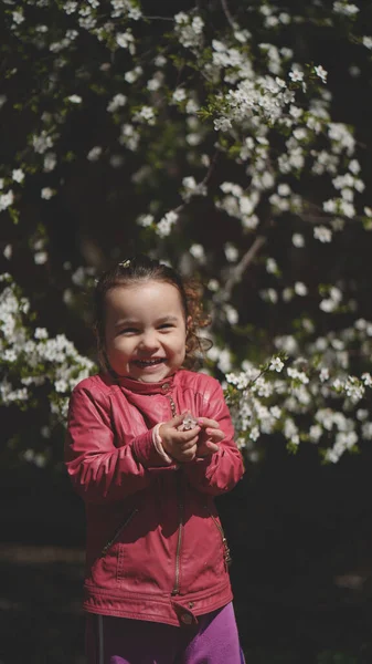 공원에서 꽃피는 나무의 가지들 사이에 귀여운 소녀의 미소짓는 — 스톡 사진