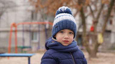 Beyaz mavi örgü şapkalı, çocuk parkında ponponlu şirin bir çocuğun portresi.