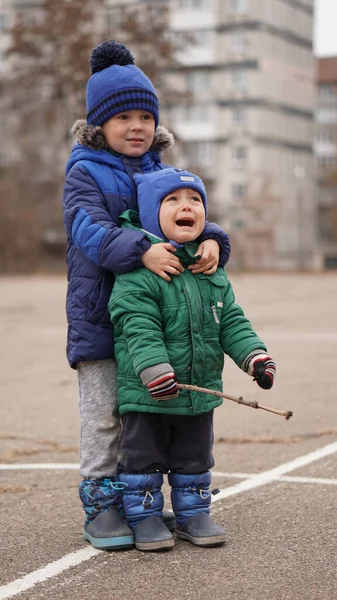 Two little boys brothers at a playground on a cloudy day. Older hugs crying little brother