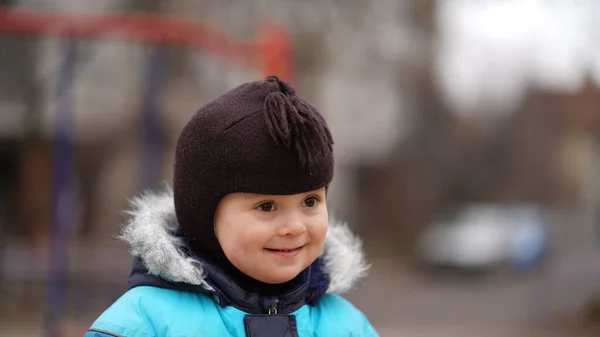 一个穿着蓝色夹克 头戴棕色帽子 面带微笑的小男孩在操场上的画像 — 图库照片