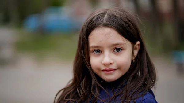 一个漂亮的小女孩的画像 她长着一头蓬松的长发 穿着蓝色夹克 在操场上的一个公园里 孩子笑得很开心 — 图库照片