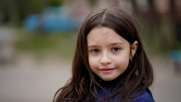 Oyun parkındaki mavi ceketli, uzun sarı saçlı güzel bir kızın portresi. Çocuk güzelce gülümsüyor