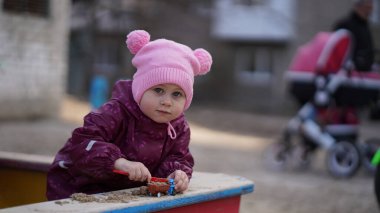 Pembe şapkalı, oyuncak arabalı şirin bir kızın portresi. Baharda Sandox 'da oyun parkında oyuncak arabayla oynuyor..