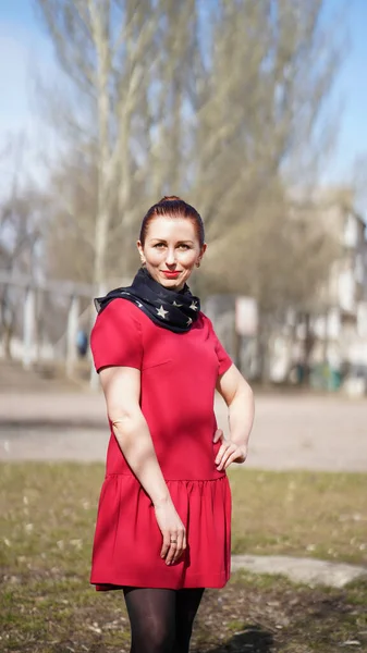 春の公園で赤いドレスを着た美しい笑顔の女性 女性のポーズとヒップに片手を保持 — ストック写真