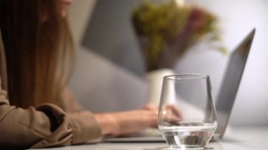 Ofis masasında çalışan genç bir kadın, belgeler ve bilgisayar. Su iç.