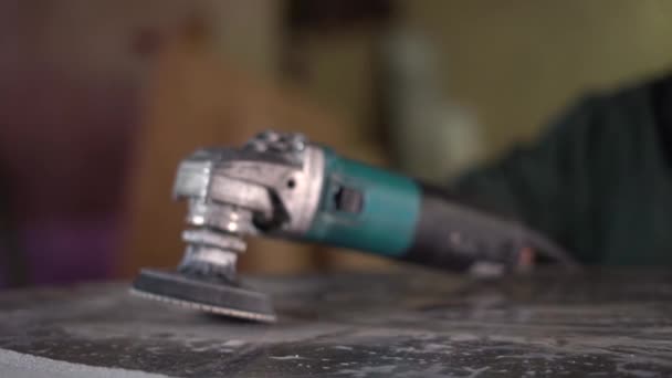 Een arbeider in een groen jasje neemt een handmatige slijper van een donker marmeren tafel in de fabriek. Super Slow Motion — Stockvideo