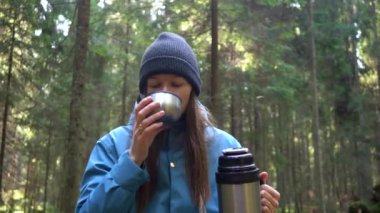 Ormandaki ağaçta oturan termostan sıcak çay içen bir kadın. Güneşli Gün